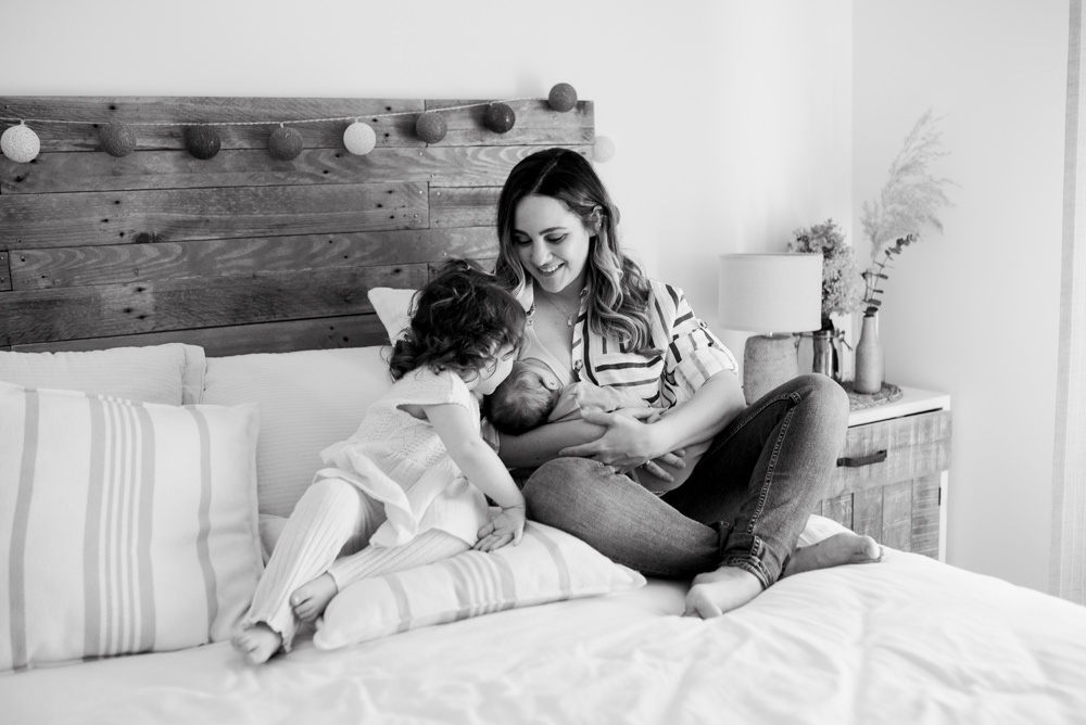 Niña besa a su hermano recién nacido mientras su madre lo alimenta. Fotografía familiar en Adra.